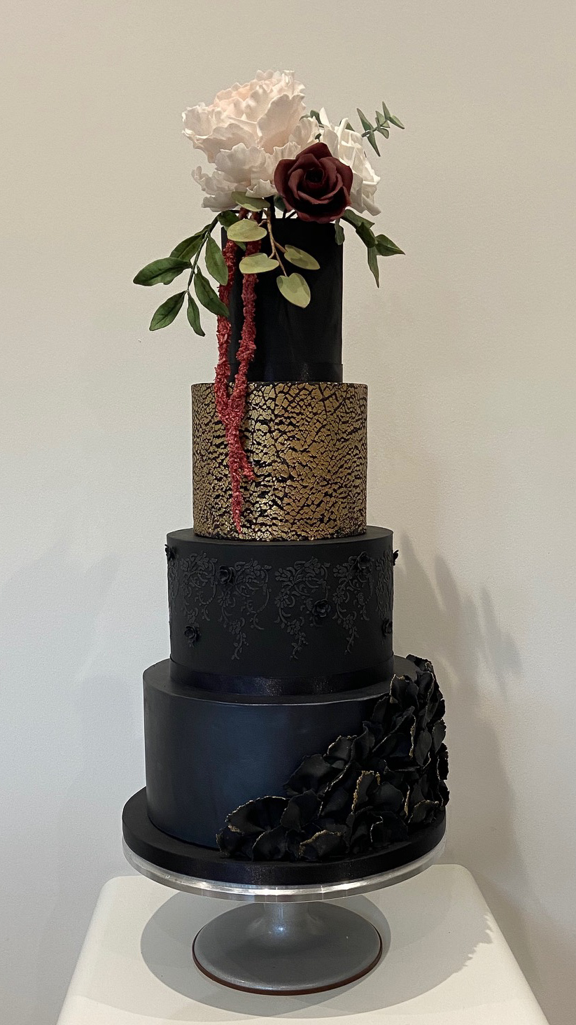 Four-tier black and gold wedding cake with textures and sugar flowers
