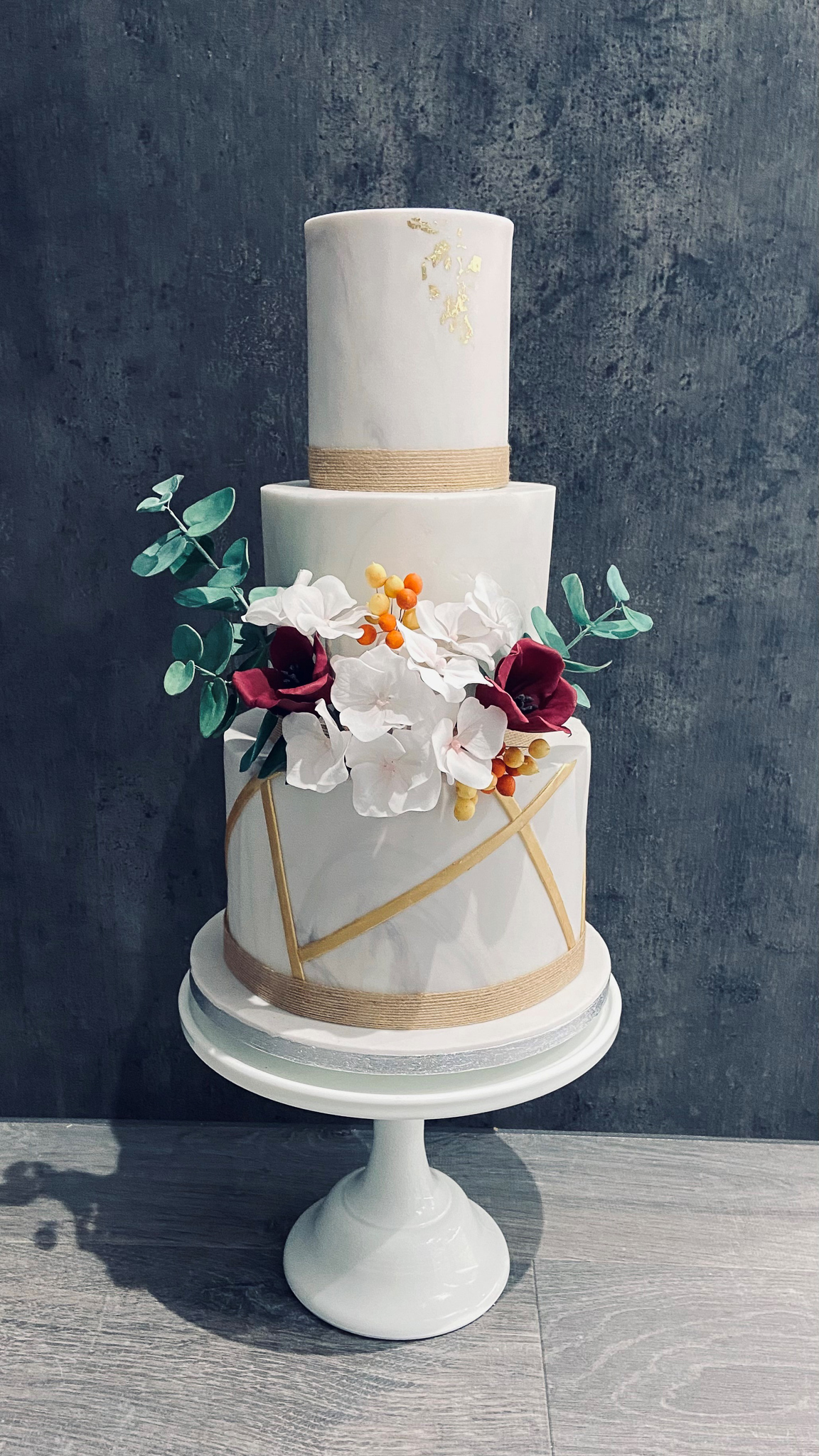 Marbled three-tier wedding cake with gold geometric design and sugar flowers